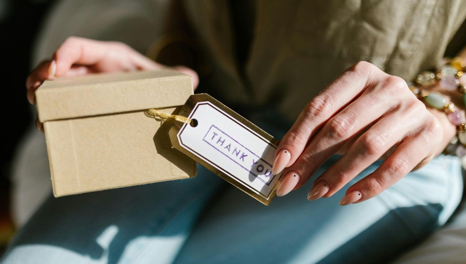 Person holding a gift box with a thank-you tag