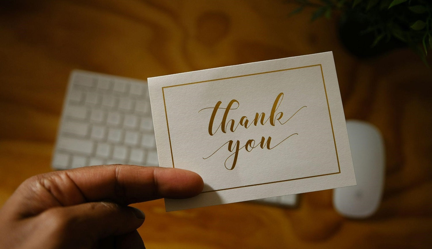 Person holding a thank-you card in front of a keyboard